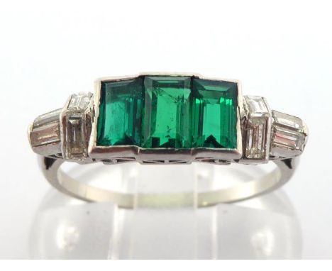 An Art Deco emerald and diamond ring, the three rectangular step cut emeralds rub over set to baguette cut shoulders, platinu