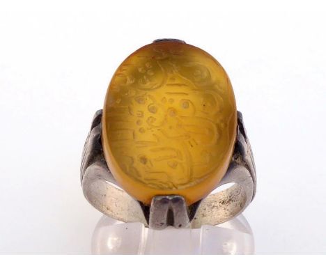 A Middle Eastern white metal (tests silver) and hardstone ring, the oval carnelian intaglio cut with Arabic text 20 x 15mm, t