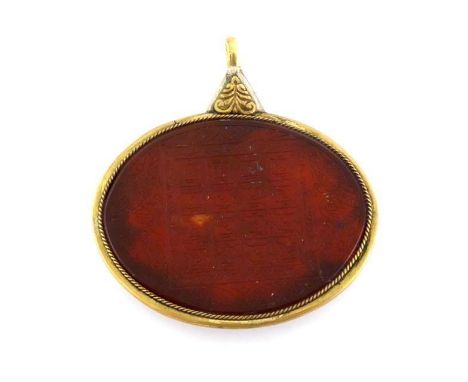 A large oval Islamic taweez, talisman, the geometric and numeric design carved on red hardstone in a brass and white metal fr