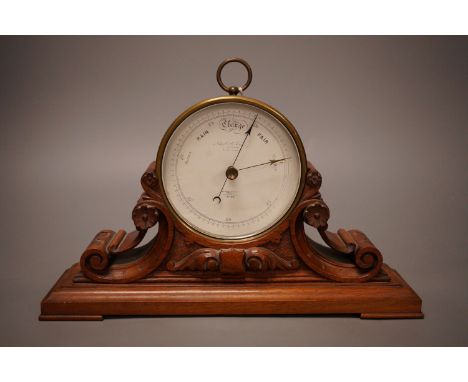 A Negretti &amp; Zambra brass cased barometer on carved mahogany stand, 31cm wide