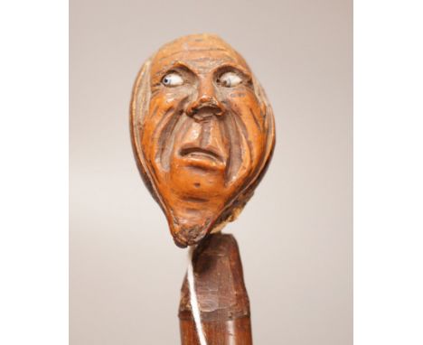 A 19th century continental carved head with glass eyes on associated cane stick. Total length 92cm