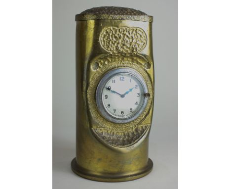 A shell case mantel clock, hammered decoration, with central mounted clock (possibly from a motor car), 24cm high