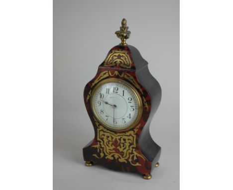 A gilt metal inlaid faux tortoiseshell mantel clock with circular white enamel dial, in baluster shaped case with finial, on 
