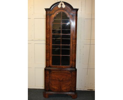 A 20th century walnut corner cabinet with broken arch top, panel glazed door enclosing four shelves with cupboard beneath, on