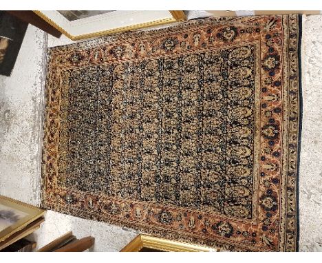 A Kashan rug, the central panel set with repeating hook motifs on a dark ground, within a stepped salmon pink, blue and musta