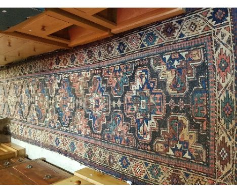 A Caucasian runner with seven repeating medallions on a dark brown ground within a stylised flower head style medallion decor