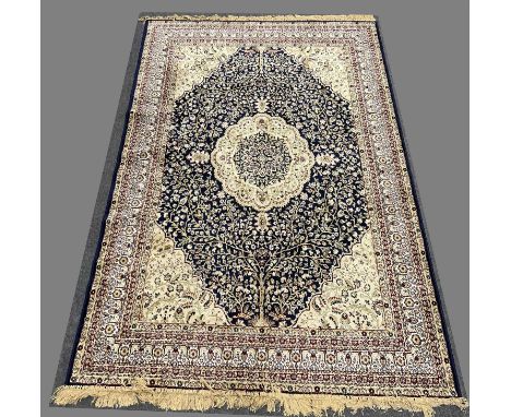 Persian silk rug, central medallion against a navy field with allover flowering trees, sand coloured spandrels, enclosed by b