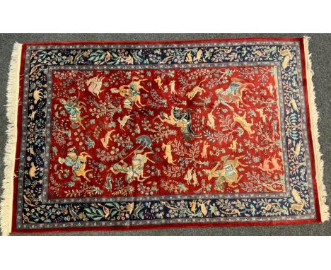 A Persian silk and wool mix rug, central panel of traditionally dressed figures on horse back fighting tigers and other anima