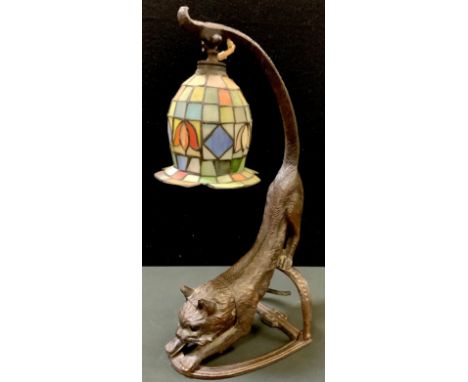 An unusual bronzed metal cat table lamp  modelled as a stretching cat with illuminated green eyes beneath a Tiffany style sha