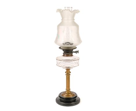 An Edwardian brass columnar oil lamp,&nbsp; with faceted glass fount and brass burner, on black glaed earthenware foot, 42cm 