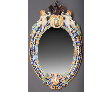 An Italian maiolica mirror, late 19th c, the oval frame surmounted by an eagle and two seated putti, 56cm h  The bevelled pla