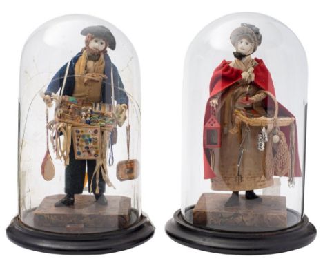 A pair of early 19th Century pedlar dolls: she in bonnet and red cloak, her wares include a lantern, bellows, fire tools, boo