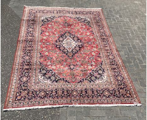 Hand-knotted Persian carpet. Colour: red, with floral border/floral decor. Dimensions: 290 x 193 cm. In good condition.