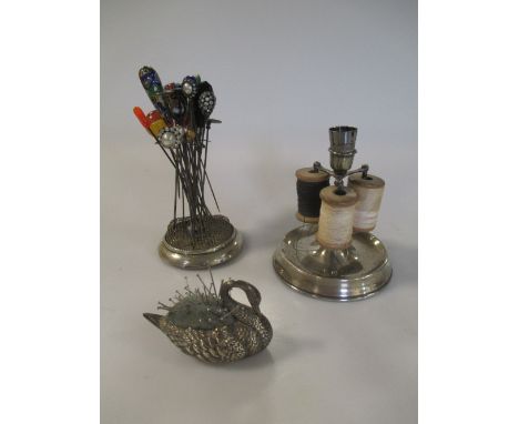 A silver swan shaped pin cushion, a silver cotton reel and thimble holder and a silver hat pin stand with a selection of hat 