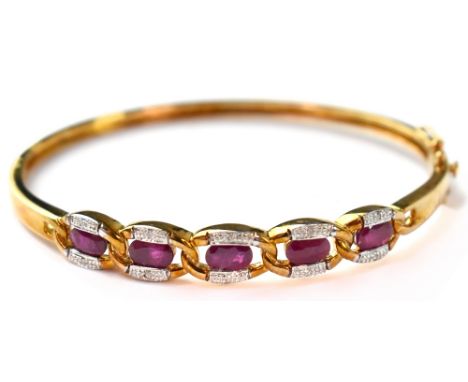 A 9ct gold diamond and ruby hinged bangle, the yellow gold bangle with five open panels with a central cushion cut ruby flank