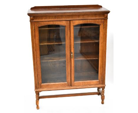 An early 20th century oak two-door display cabinet with simple frieze decoration above pair of arched glazed doors and raised