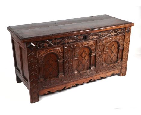 An 18th century oak coffer, the three-panel front heavily carved with leaves, Gothic type arches and scrolls, on stile legs, 