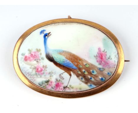An oval porcelain panel brooch hand painted with a peacock within flowers, in a 9ct gold mount.