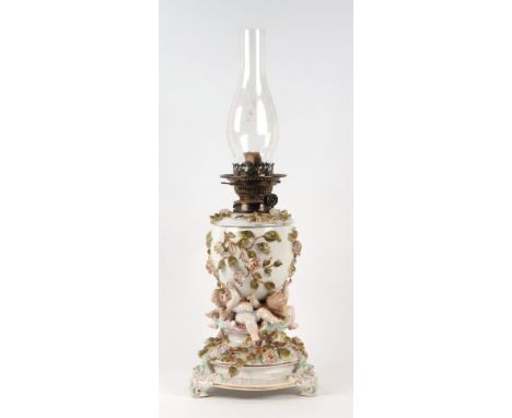 A Sitzendorf type continental porcelain oil lamp, the reservoir decorated with applied scrolling roses and supported by three