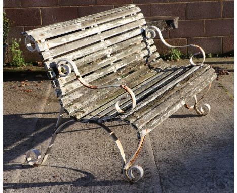 A slatted wooden garden bench with wrought iron scroll arms and feet, 153cms wide.