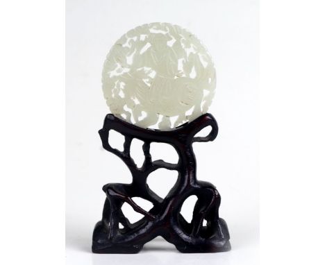 A Chinese pierced and carved celadon  jade roundel depicting a boy on a lion; together with a carved hardwood stand modelled 