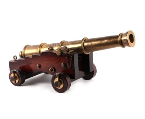 A brass or bronze cannon mounted on a wooden carriage with brass/bronze fittings and a wooden wedge. The barrel having a leng