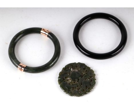 A Chinese green jade bangle with gold metal mounts (tested), 7.5cms diameter; together with a pierced jade roundel and a blac