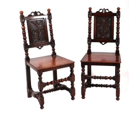 A pair of Victorian oak hall chairs in the 16th century style with carved back panels, solid seats and bobbin turned legs and