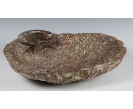 A 20th century carved stone bowl, roughly hewn from cretaceous rock, the rim with integral ammonite specimen, width 42cm.