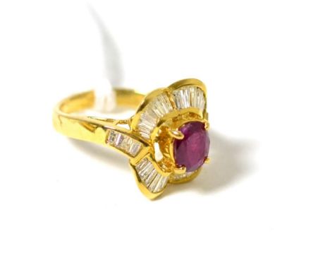 A ruby and diamond cluster ring, an oval cut ruby in a yellow claw setting within an undulating border of tapered baguette cu