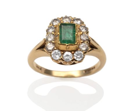 An 18ct gold emerald and diamond cluster ring, an emerald-cut emerald in a yellow rubbed over setting, within a border of rou