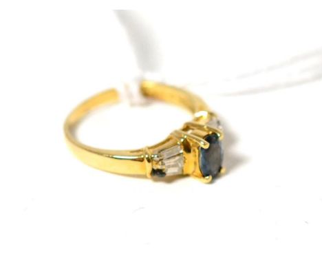 A sapphire and diamond ring, an oval cut sapphire in a yellow four claw setting, to tapered baguette cut diamond shoulders, o