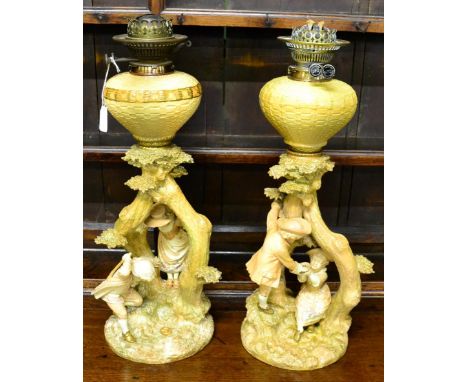 A pair of Royal Worcester oil lamp bases, modelled as children playing amongst trees, 49cm high, with fittings      