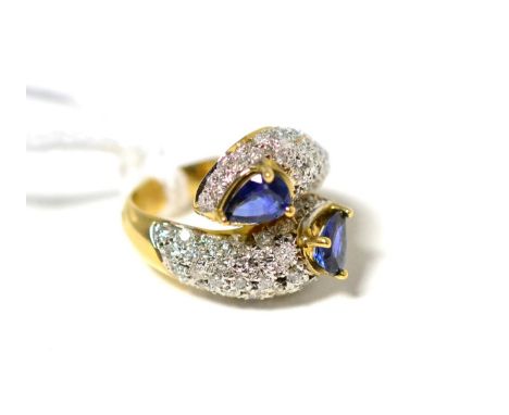 A sapphire and diamond twist ring, two pear cut sapphires in yellow claw settings to pavé set round brilliant cut diamond twi