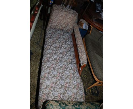 A light oak framed chaise longue on turned legs with carved shell detail, upholstered in floral fabric.