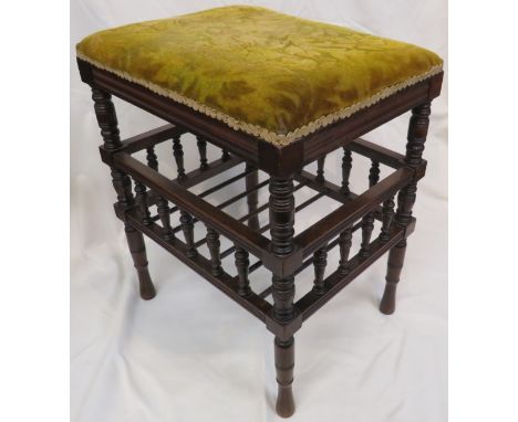 An Edwardian upholstered red walnut stained piano stool with a lower bobbin gallery and open music shelf on turned legs