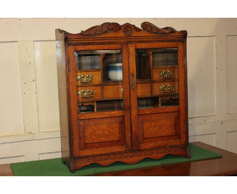 An early 20th century oak smokers cabinet, the two bevelled glass panel doors enclosing an arrangement of drawers and shelves