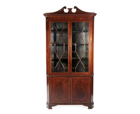 A Late George III Mahogany Free-Standing Corner Cabinet, circa 1800, the broken swan neck pediment above a dentil cornice, in