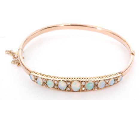 AMENDED DESCRIPTION - A 9ct rose gold synthetic opal and diamond hinged bangle, nine oval cabochons spaced by pairs of round 