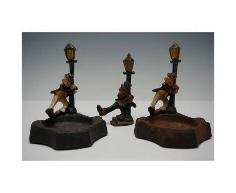 A set of three antique cast iron figural pieces featuring a humorous "drunkard" theme. Two of the pieces serve as ashtrays, w