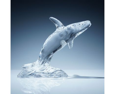 Clear crystal figurine depicting a humpback whale leaping out of the water. The design features detailed contouring along the