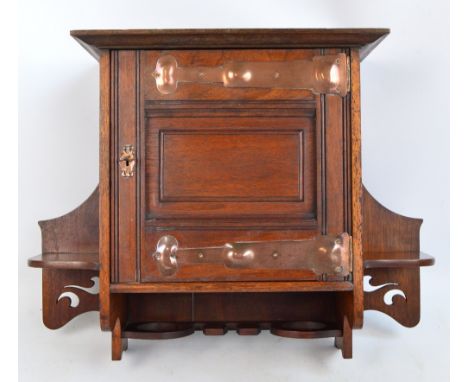 A c.1900 Arts and Crafts mahogany wall mounted smoker's cabinet with broad copper strapwork hinges, the moulded door enclosin