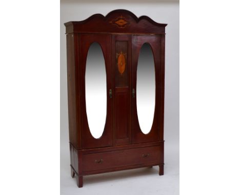 An early 29th century mahogany wardrobe with shaped inlaid pediment above two hinged doors set with oval bevelled mirrors div