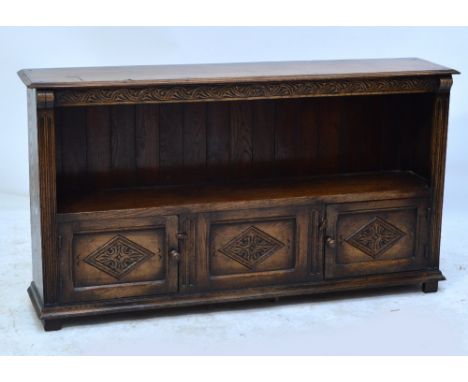 A reproduction oak low bookcase with carved frieze above shelf with panel back above two hinged doors with lozenge carving an