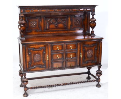 An early 20th century oak side table with carved back, urn shaped supports, three central drawers flanked by hinged doors, on