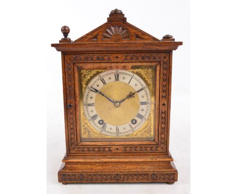 An Edwardian oak cased eight day mantel clock with shaped top above single glazed door with carved decoration, the silvered d