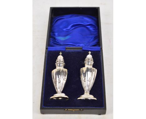 A cased pair of Edward VII hallmarked silver urn shaped peppers with fluted corners raised on oval domed base with pierced co