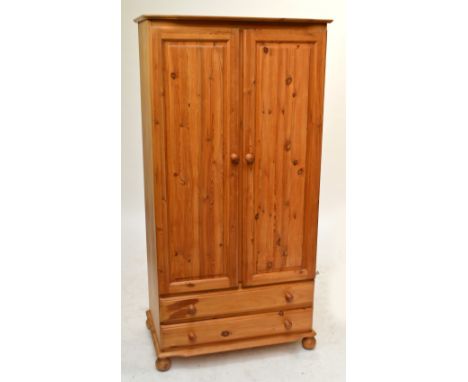 A pine wardrobe with pair of doors enclosing a shelf and a rail rack above two long drawers and turned bun feet, height 183cm
