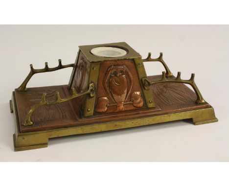 An Arts and Crafts copper and brass desk stand, the central spreading square inkwell embossed to each side with an owl, flank