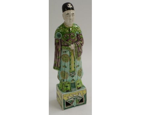 A Chinese famille verte porcelain figure, of an Immortal, standing in flowing robes on a square base, the sides of which are 